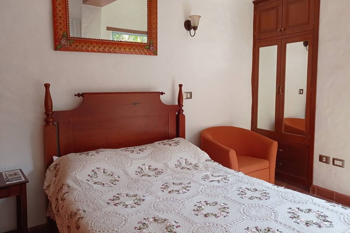 A bedroom with a wooden bed, a chair, a wardrobe, and a mirror on the wall.