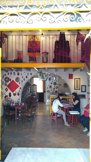 Un café à deux étages, doté d’un intérieur dynamique, avec différents types de mobilier et des éléments décoratifs tels que des miroirs et des œuvres d’art mural.