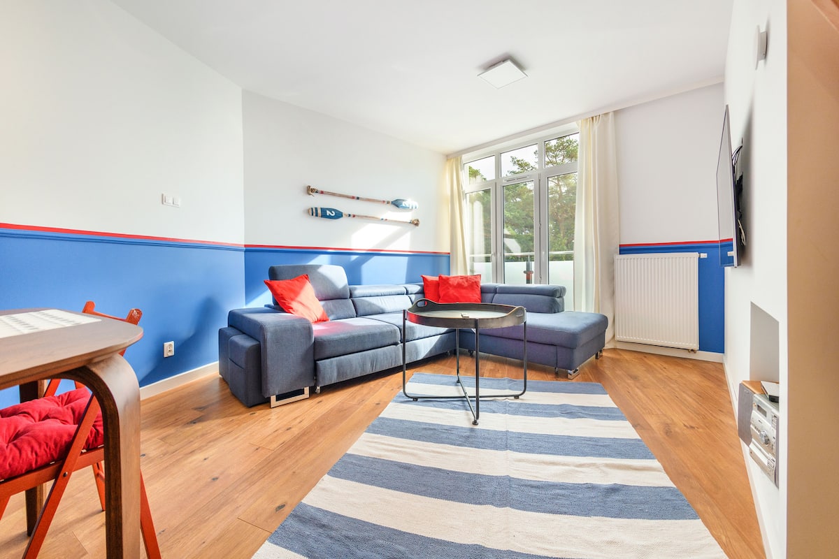 A modern living room with a blue sofa, a dining table, and a striped rug.