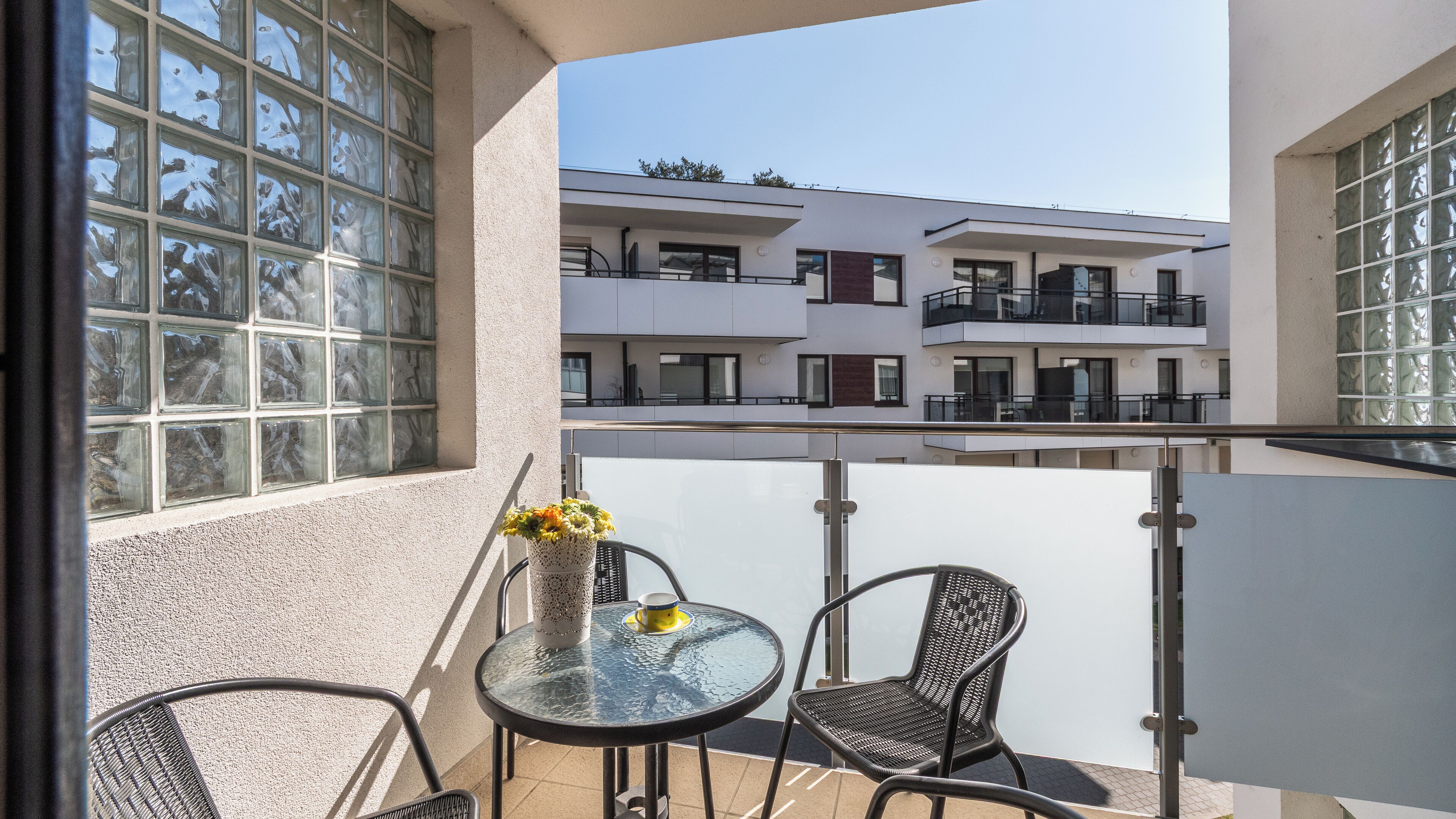 Ein Balkon mit Glastisch, zwei Korbstühlen und einer Blumenvase.
