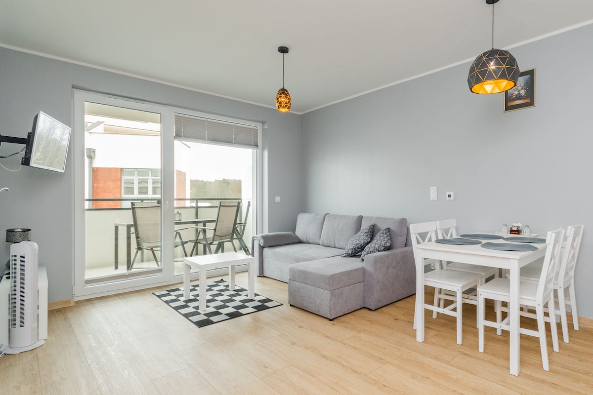 A modern living space with a grey sofa, a dining table with chairs, a black and white checkered rug, and a ceiling light fixture.