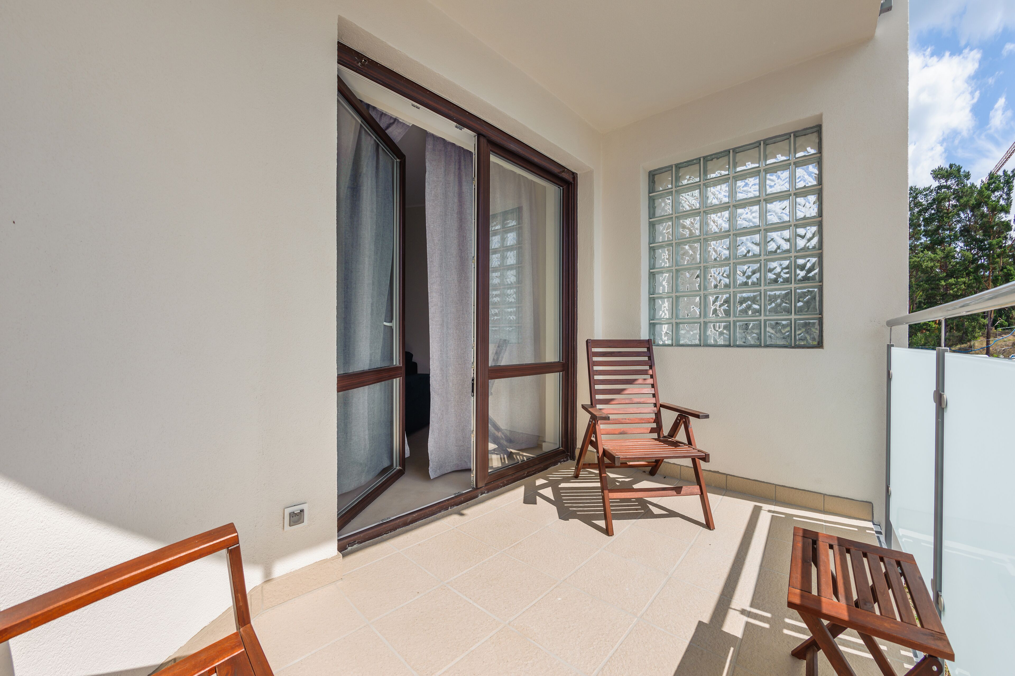 A balcony with a wooden chair, a table, and a window with a grid pattern.