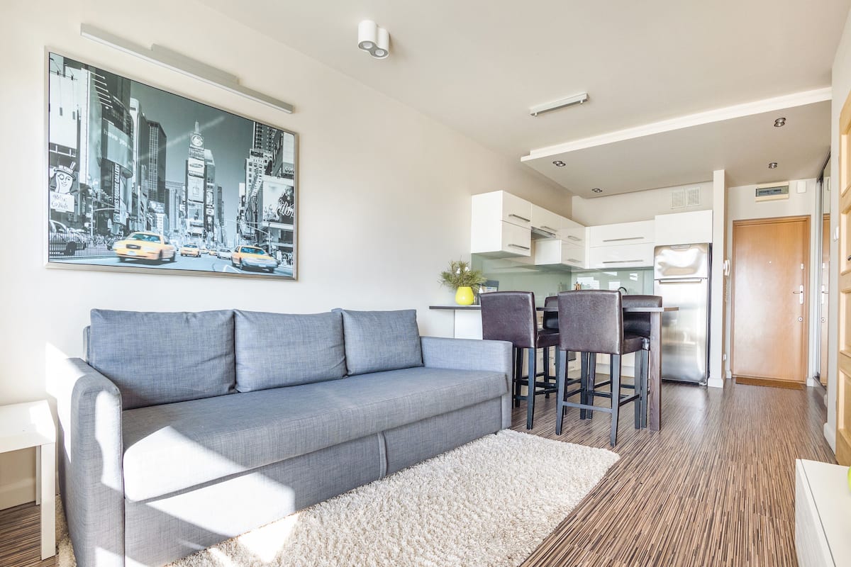 A modern living room with a grey sofa, a coffee table, and a cityscape painting.