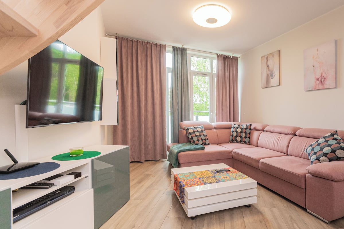 A modern living room with a sectional sofa, a flat-screen TV, a coffee table, and a TV stand with a remote control.