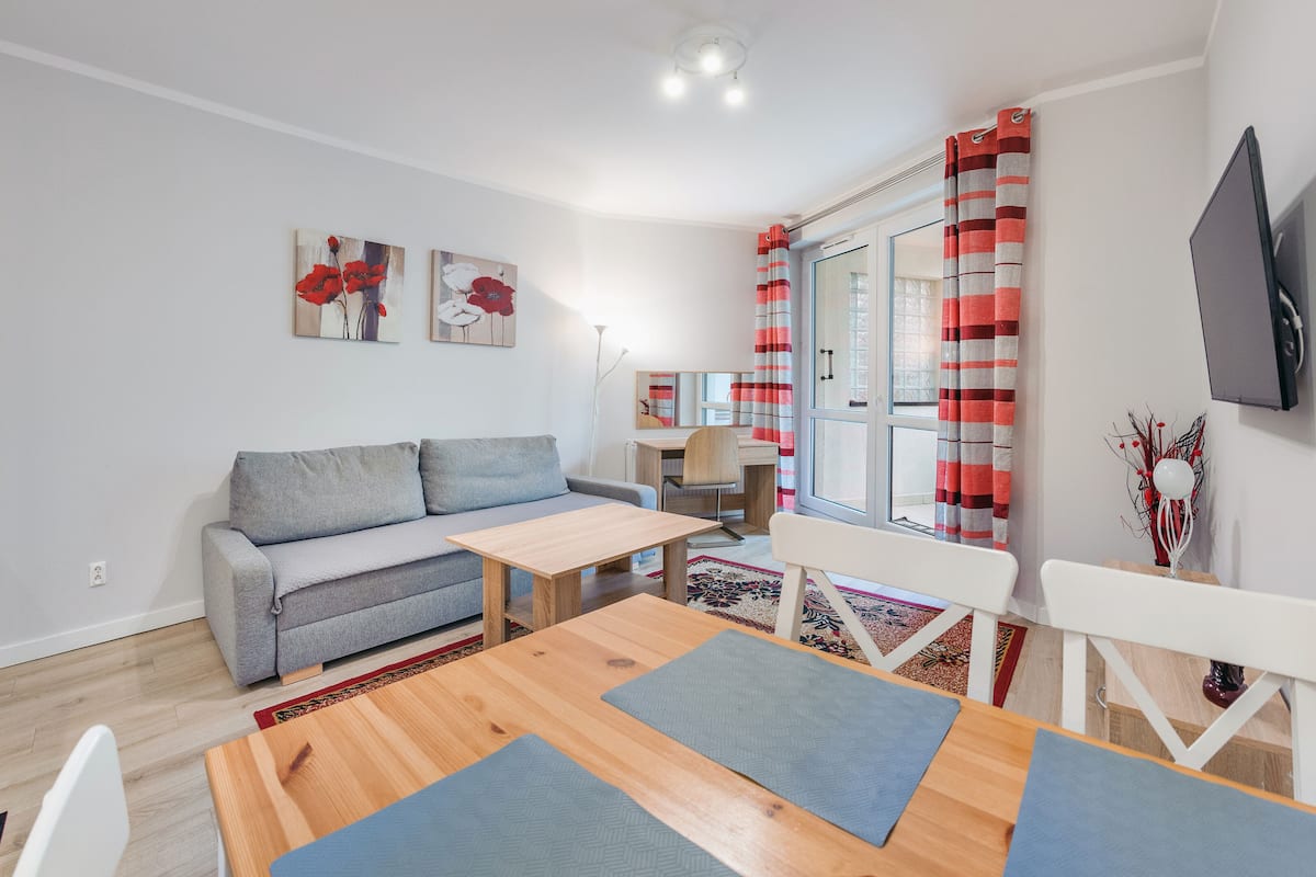 A modern living room with a grey sofa, wooden coffee table, and a dining area with a white table and chairs.