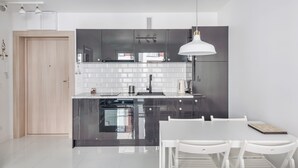 Una cocina moderna con una isla central, salpicadero de azulejos blancos, muebles oscuros y una lámpara colgante blanca.