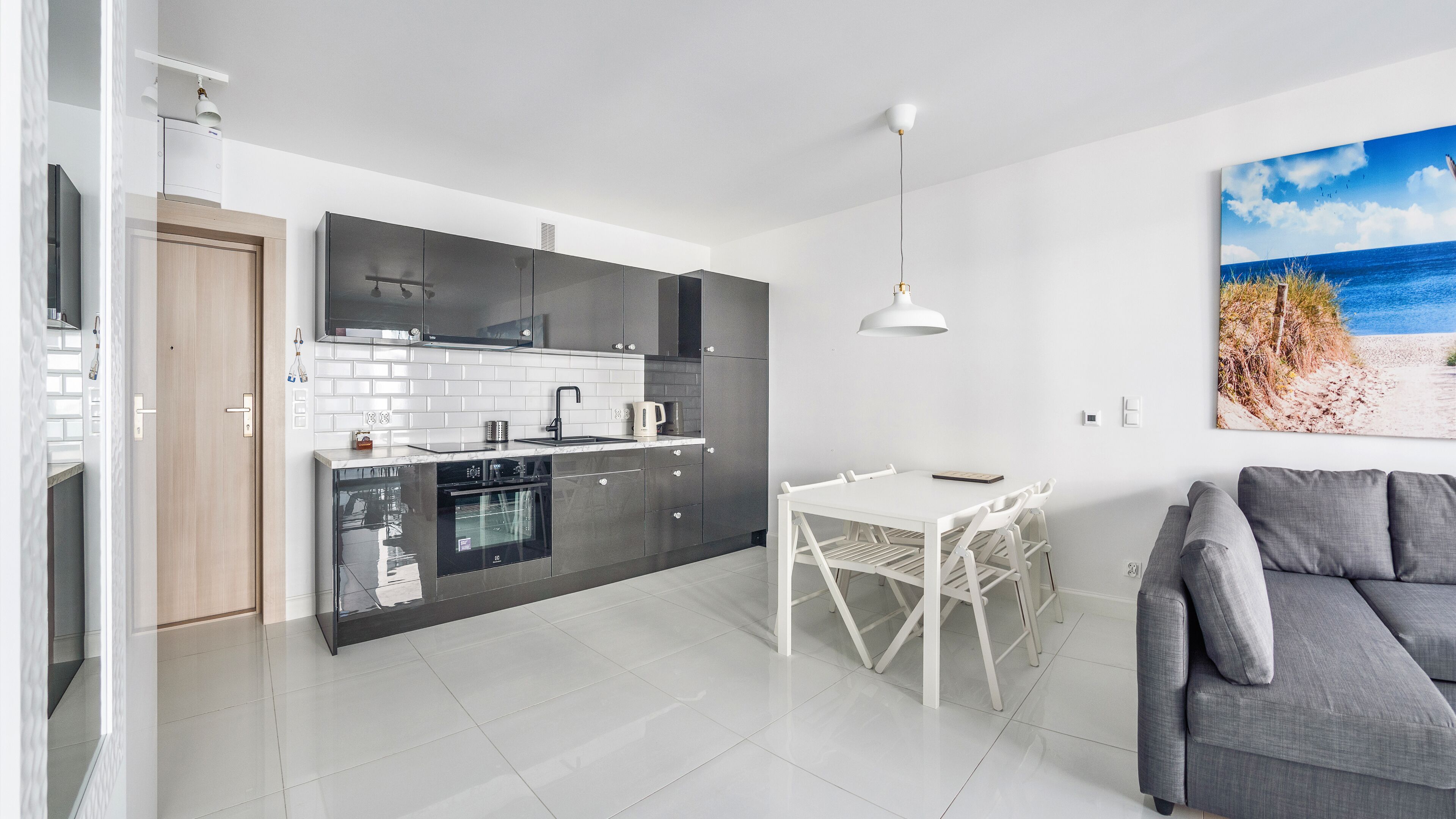 Una cucina moderna con zona pranzo, un divano grigio e un quadro con vista mare.
