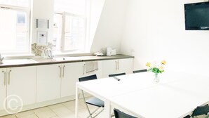 A bright kitchen with white cabinets, a window, and a dining table with chairs. - Cricklewood Studio Flats (London)