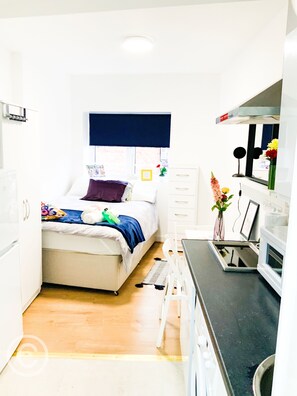 A compact bedroom with a bed, bedside table, and a small kitchenette.
