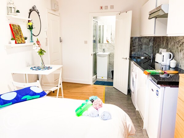 A compact hotel room with a bed, a small desk, a bathroom, and a kitchenette.
