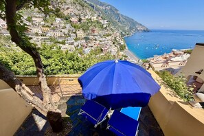 Une terrasse avec un parasol bleu, un arbre et une vue sur une ville côtière.