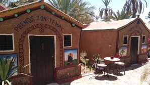 A building with a sign reading "PRENDOS TON TEMPS" and another sign "TOMA TU TIEMPO". There are two doors, one with a window, and a small patio area with a table and chairs. - Hostel take your time 4225 (Zagora)