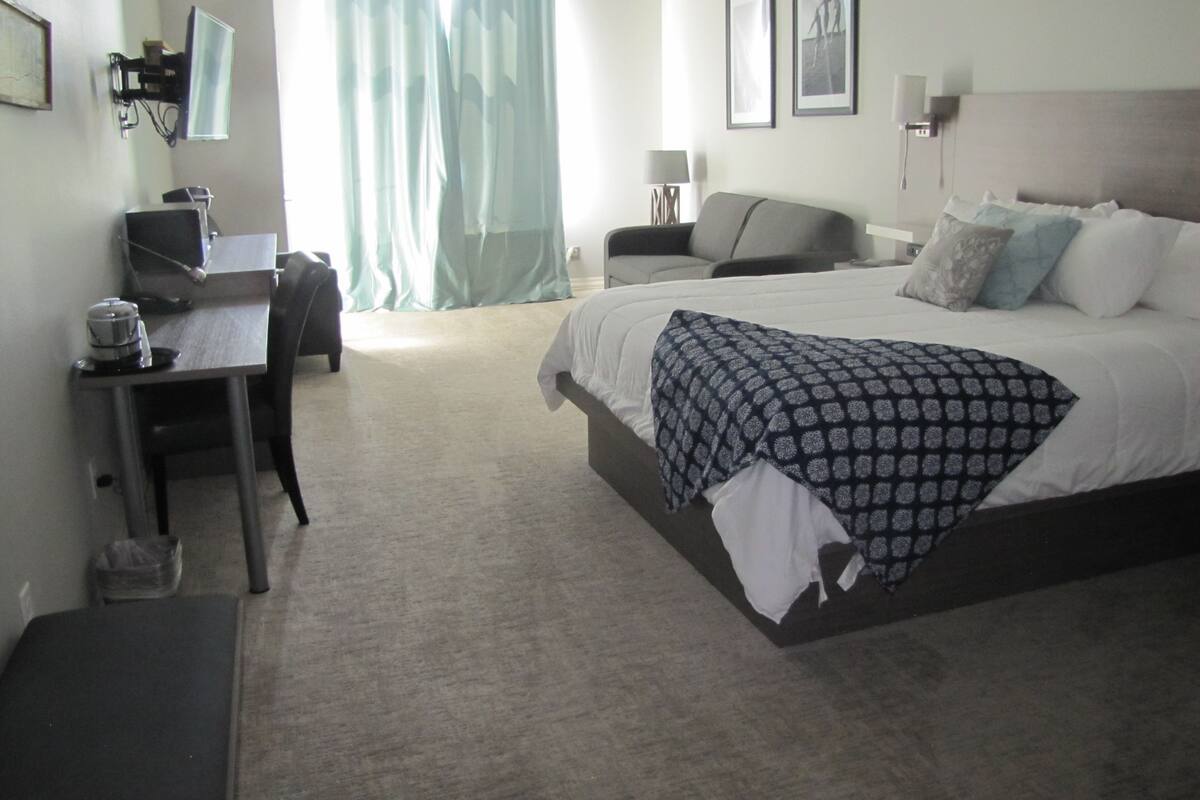 Une chambre d’hôtel avec un lit, un bureau, une chaise, une lampe et un téléviseur.