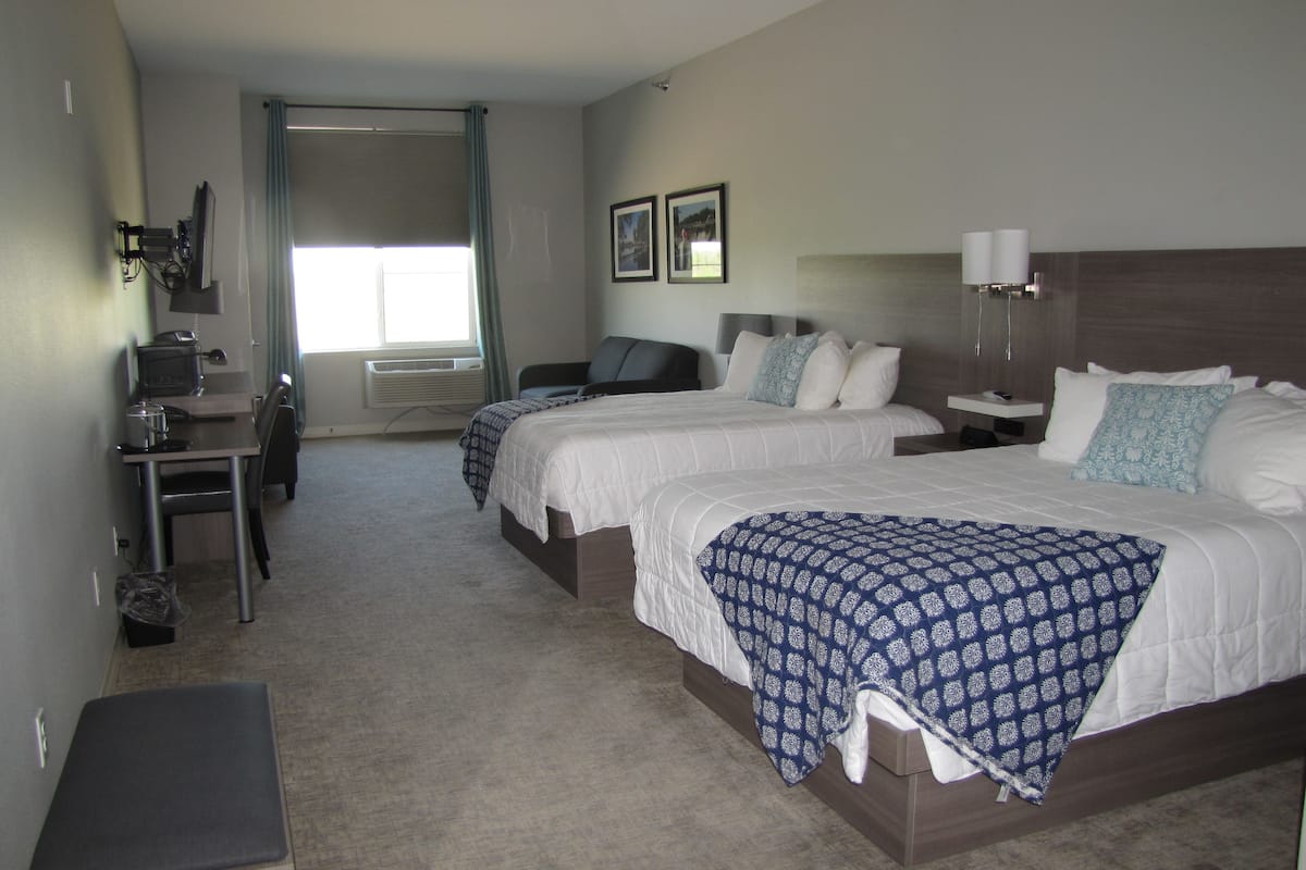 Une chambre d’hôtel avec deux lits, un bureau, une chaise, une petite table et une fenêtre avec des rideaux.