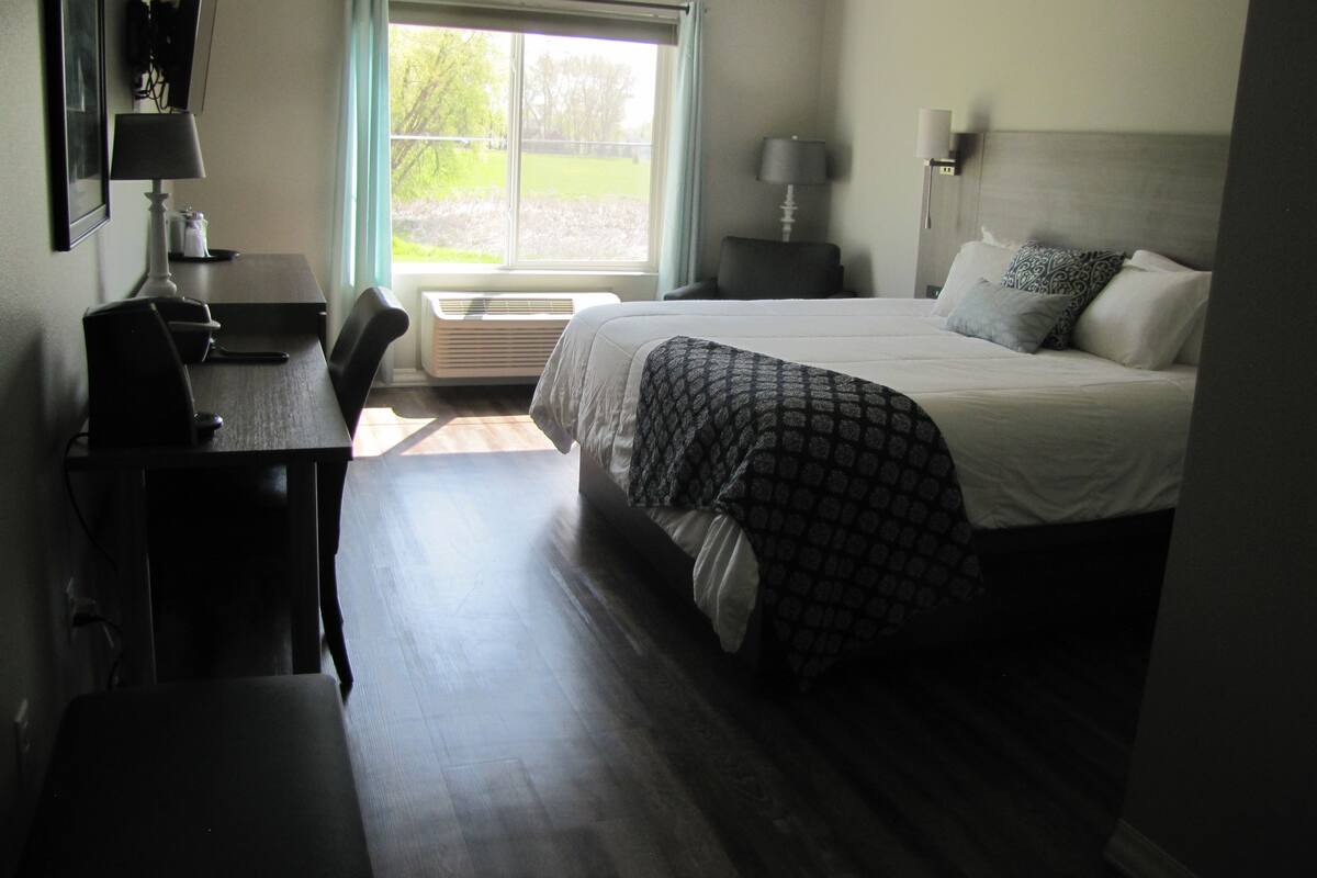 Une chambre d’hôtel équipée d’un lit, d’un bureau, d’une chaise, d’une fenêtre avec des rideaux et d’une lampe fixée au mur.