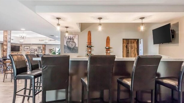 A modern bar area with black leather bar stools, pendant lighting, and surfboards on the wall. - Lakes Inn at Dunvilla (Pelican Rapids)