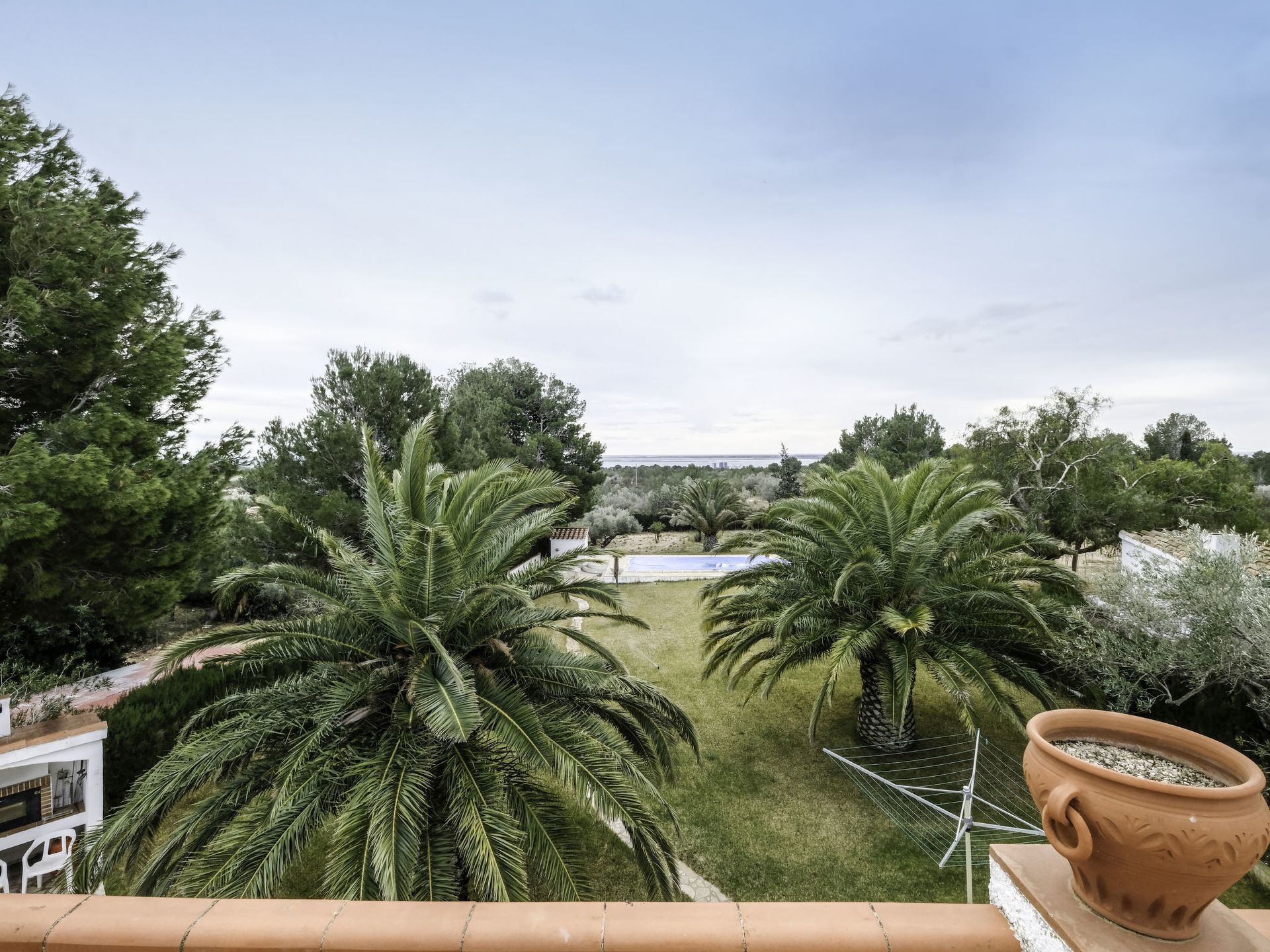 A balcony with a view of a garden featuring palm trees and a white building in the background.