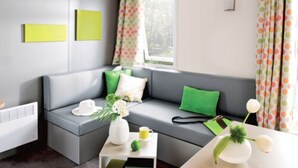 En moderne stue med en grå sofa, grønne puder, en hvid vase med blomster og et lille bord med en kop.