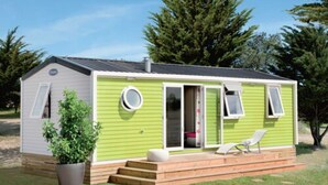 En mindre, etetages campingvogn med grøn facade, en veranda med bænk og en potteplante.
