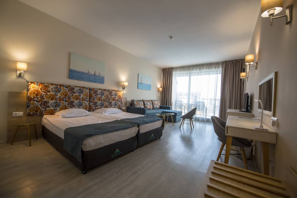 Ett hotellrum med en stor säng, ett skrivbord, en stol, ett litet bord och en TV.