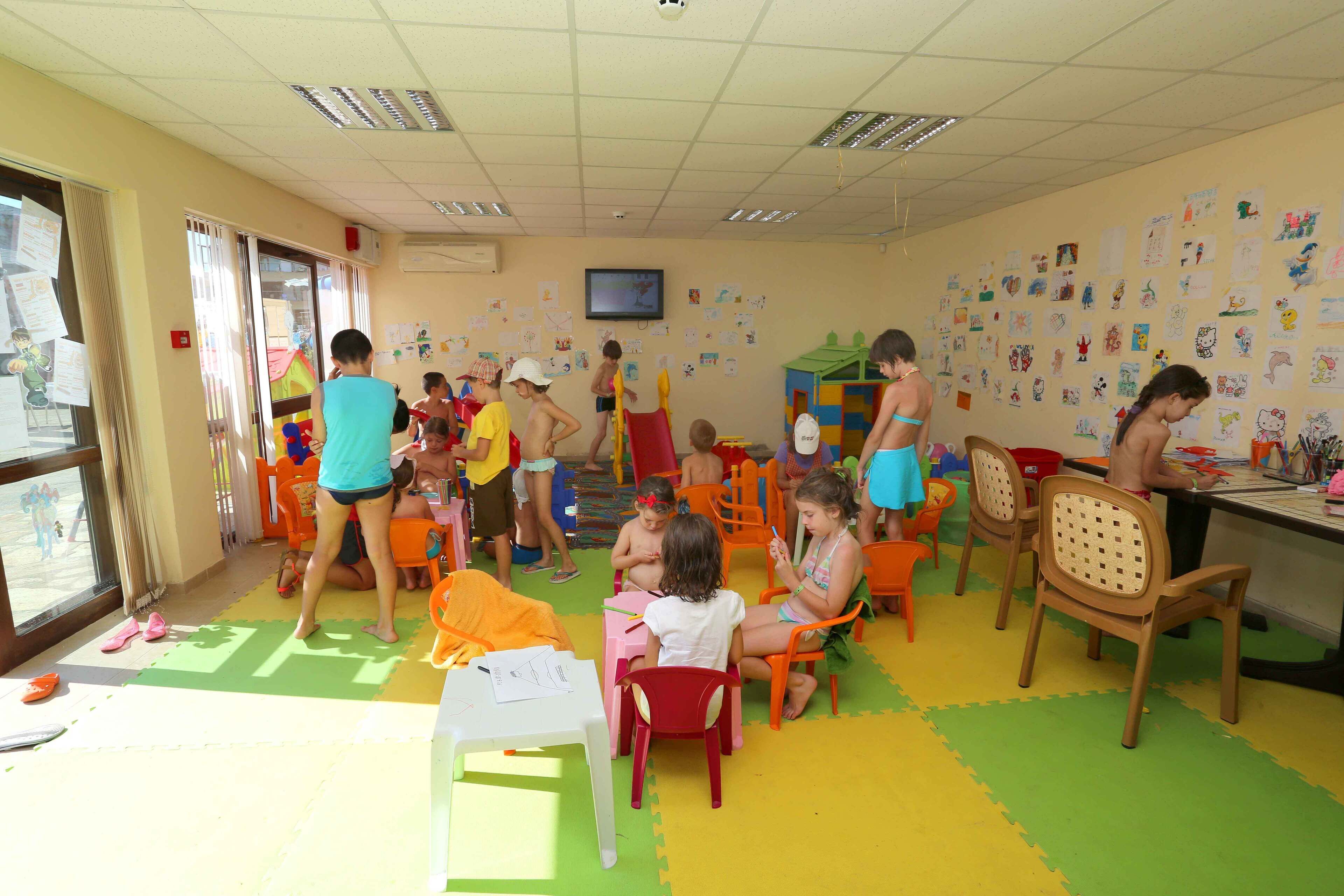 Ein Klassenzimmer mit Kindern bei verschiedenen Aktivitäten, bunten Matten auf dem Boden und lehrreichen Postern an den Wänden.