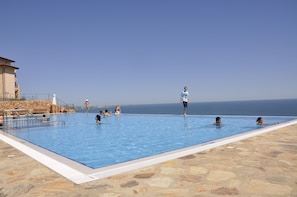 A swimming pool with a stone deck, a building with a balcony, and a view of the sea. - Topola Skies Resort & Aquapark - All inclusive (Kavarna)