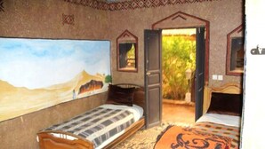 A room with two single beds, a large painting of a desert landscape, and a door leading to an outdoor area with greenery. - Hostel take your time 4235 (Zagora)