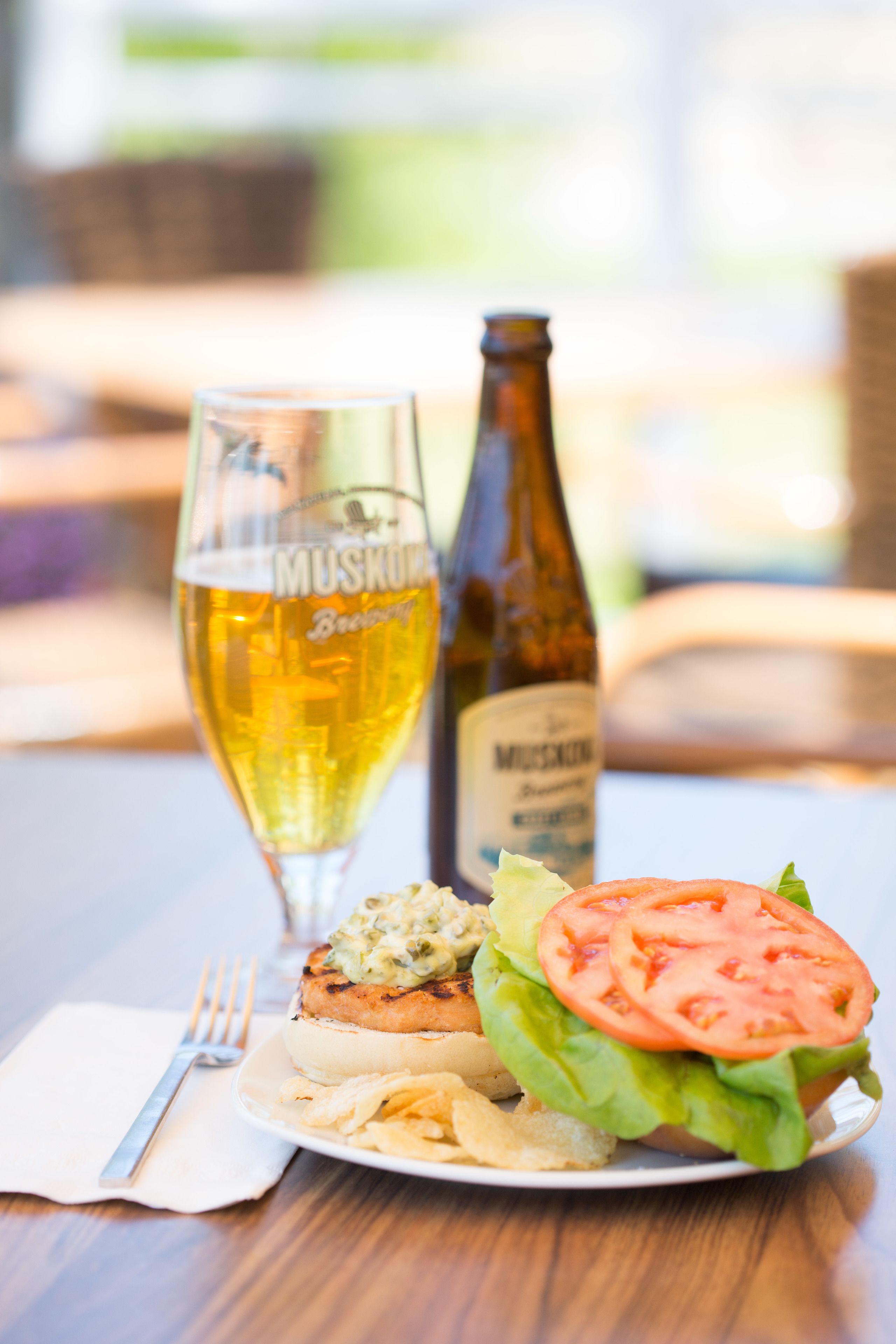 A meal with a burger, a glass of beer, and a bottle of beer on a table.