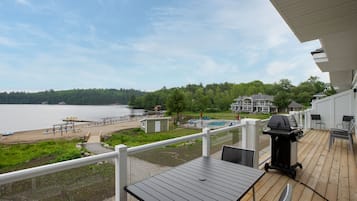 Relax on the deck with a table and chairs, overlooking a serene lake and distant shoreline.