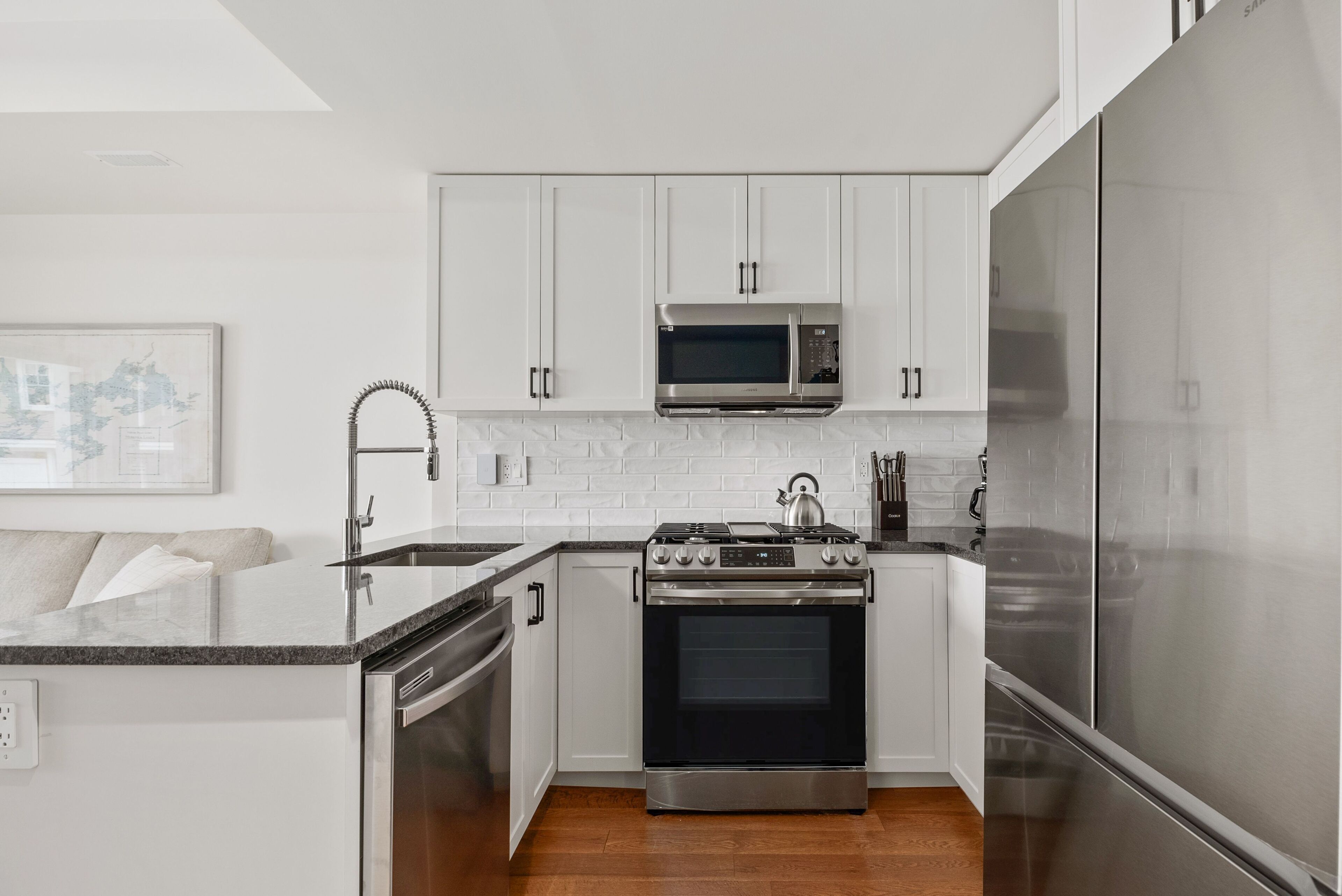 A modern kitchen with white cabinets, stainless steel appliances, and a wooden floor.