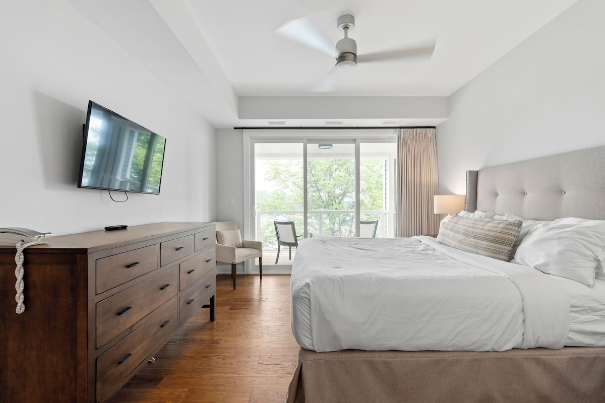 A bedroom with a bed, a dresser, a TV, and a ceiling fan.