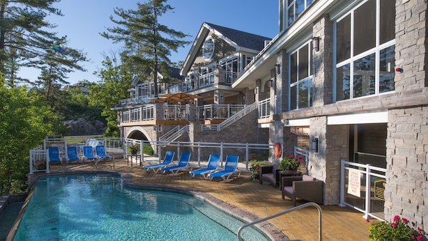 A pool area with lounge chairs, a staircase to a balcony, and a view of trees. - Touchstone Resort (Muskoka Lakes)