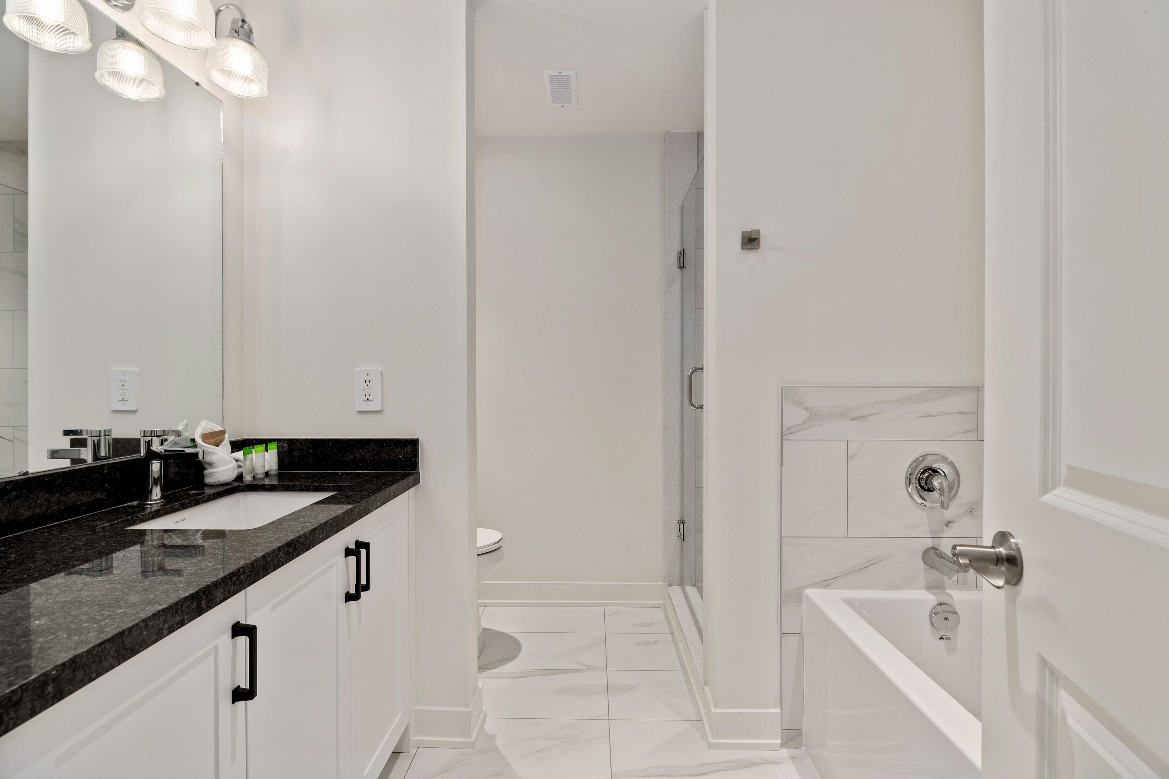 Une salle de bain moderne avec un plan de toilette noir, des meubles blancs, un grand miroir et un espace douche.