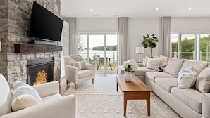 A modern living room with a stone fireplace, comfortable seating, and large windows offering a view of greenery. - Touchstone Resort (Muskoka Lakes)