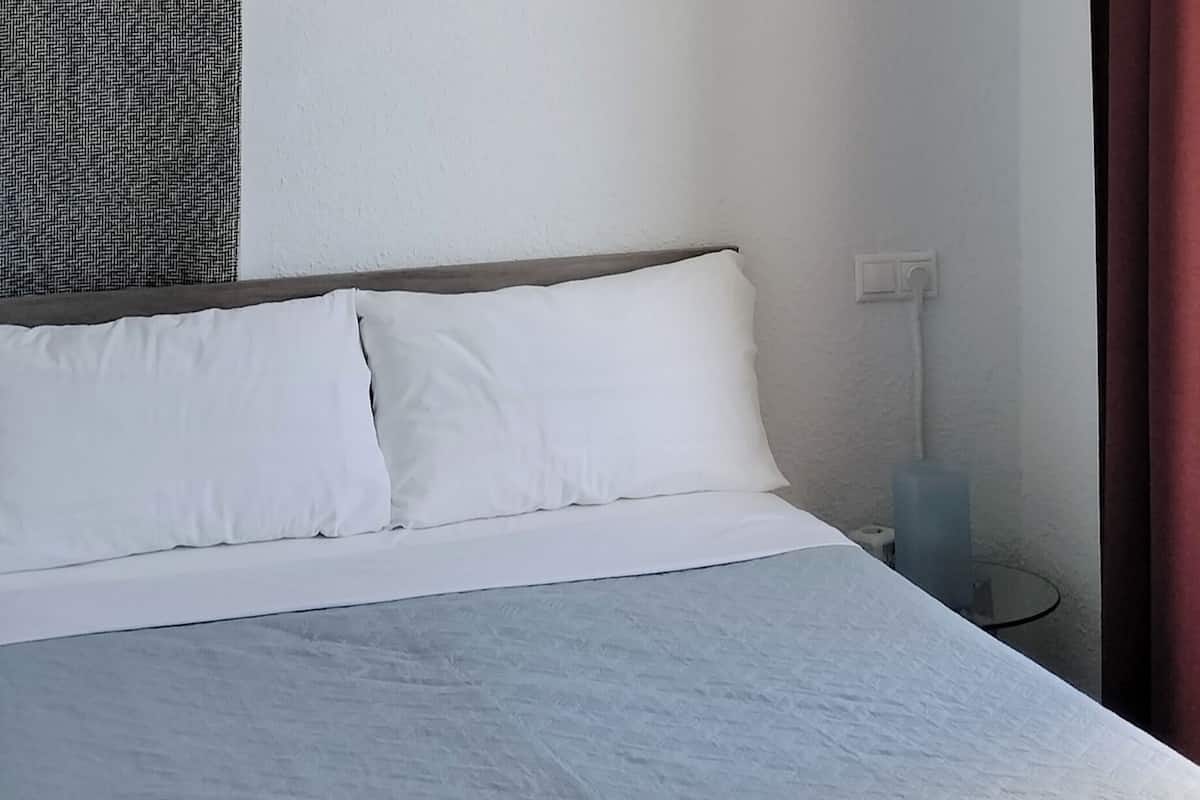Siististi pedattu sänky valkoisilla lakanoiden kanssa, yöpöytä lampulla ja punainen verho.