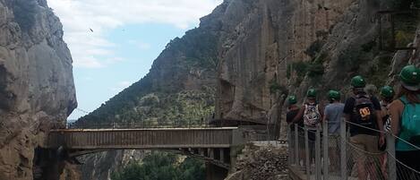 Un puente colgante sobre un cañón, con un río serpenteando abajo, rodeado de acantilados rocosos.