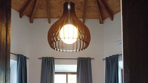 Un dormitorio con techo de madera, un ventanal con cortinas, una cama con sábanas blancas y una lámpara colgante.