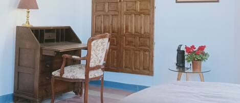 Une pièce comprenant un bureau en bois, une chaise, un lit, une lampe, une affiche et une petite table sur laquelle est posée une plante en pot.