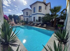 Una piscina al aire libre, sombrillas, sillones reclinables de piscina
