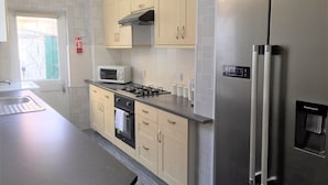 A modern kitchen with beige cabinets, a stainless steel refrigerator, a microwave, a gas stove, and a water dispenser.