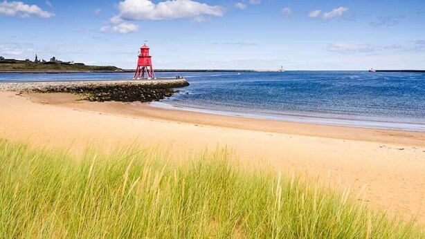 A beach with a red lighthouse, clear skies, and calm waters.