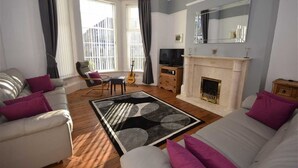 A living room with a fireplace, a sofa set, a television, and a guitar.