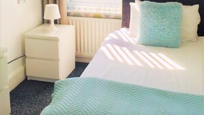 A hotel room with a bed, a nightstand, a lamp, a window with blinds, and a patterned wall.