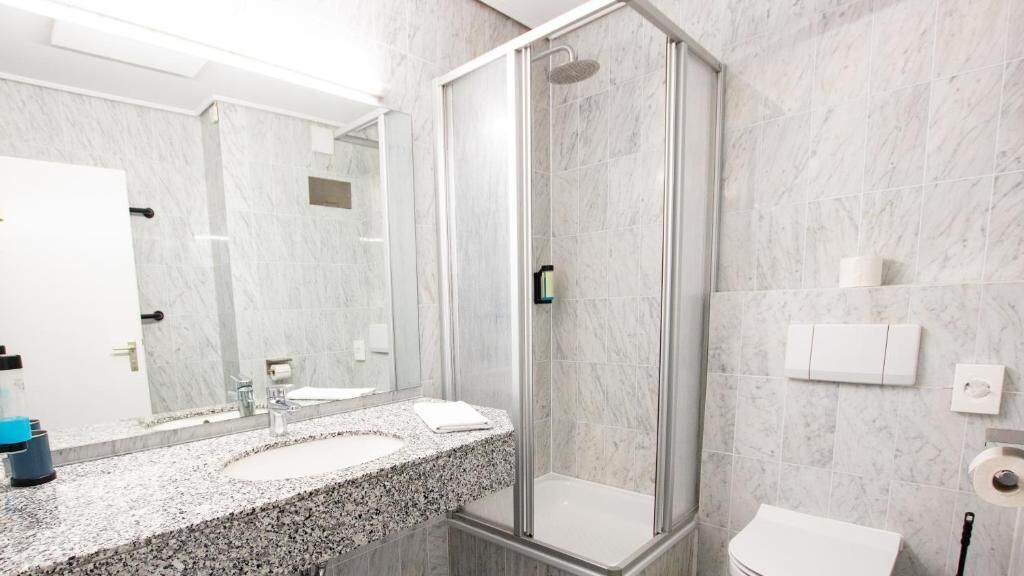 Un baño moderno con cabina de ducha de vidrio, pared con azulejos de mármol, lavabo con encimera de granito y un inodoro.
