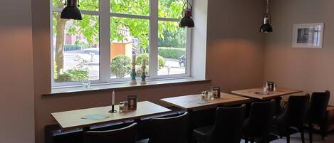A restaurant with a large window, multiple tables, and black chairs.
