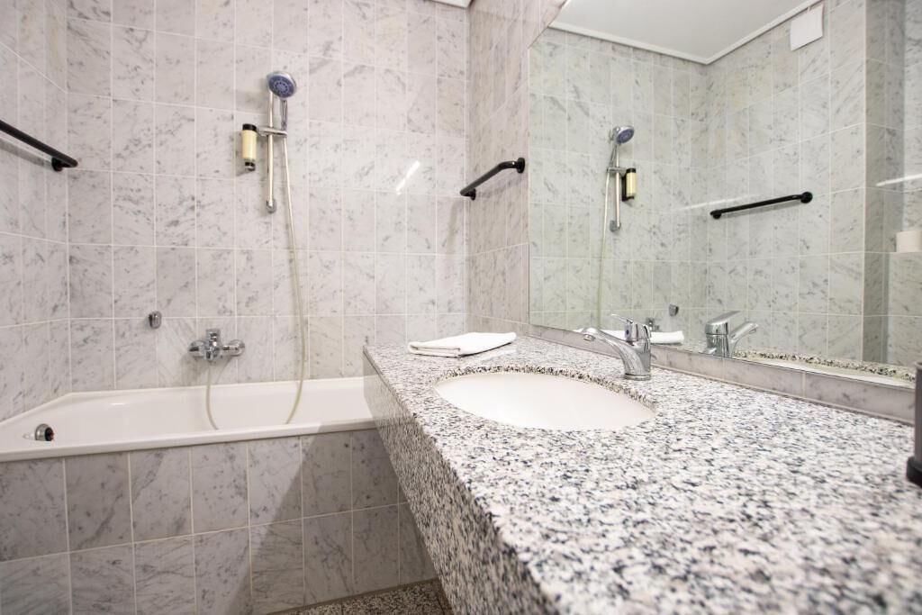 A bathroom with a bathtub, a sink with a granite countertop, and a large mirror.