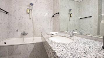 A bathroom with a bathtub, a sink with a granite countertop, and a large mirror.