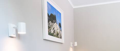 A neatly made bed with a grey headboard, a framed picture on the wall, and a small wooden nightstand.