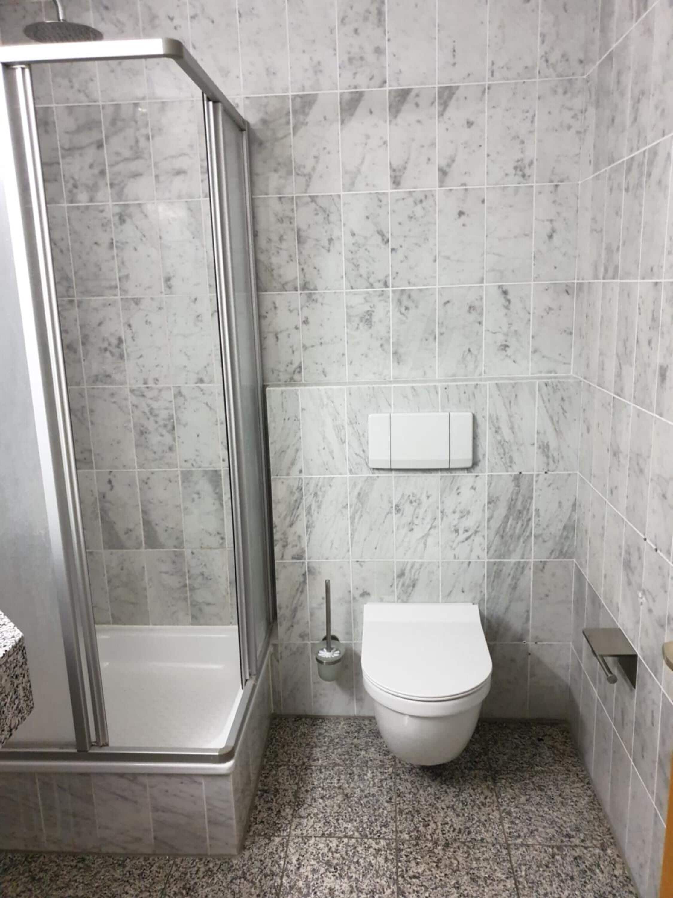 Une salle de bain avec une douche, des toilettes et des carreaux de marbre.