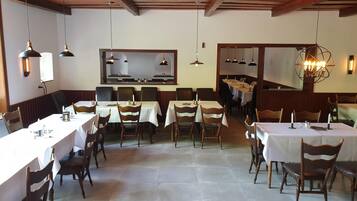 Un restaurant doté de nombreuses tables et chaises, de poutres en bois au plafond et d’un éclairage suspendu.